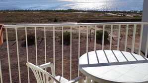 Un balcon avec une table et une chaise blanches, donnant sur une étendue d’eau et une côte lointaine.