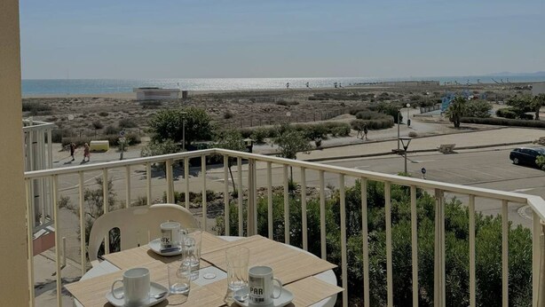 Un balcón con una mesa lista para dos personas, con vista a una playa y un estacionamiento.
