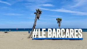 Una playa con palmeras y un letrero que dice '#LE BARCARES'.