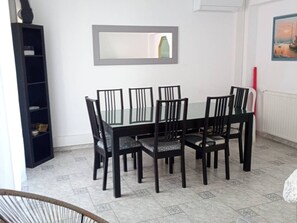 A dining area with a rectangular table and six chairs, a black bookshelf, and a framed picture on the wall. - Village house with air conditioning, terrace, 6-8 pers, Canet-en-Roussillon (Canet-en-Roussillon)
