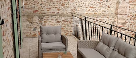 Un patio con paredes de piedra, muebles de mimbre, una mesa de madera y una barandilla de metal.
