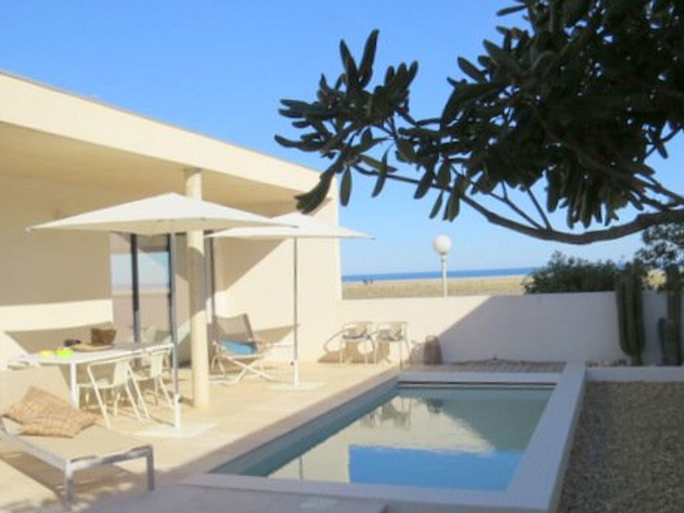 Un espace piscine extérieur moderne, doté de chaises longues et de parasols, offrant une vue dégagée sur la mer et présentant un design architectural minimaliste.