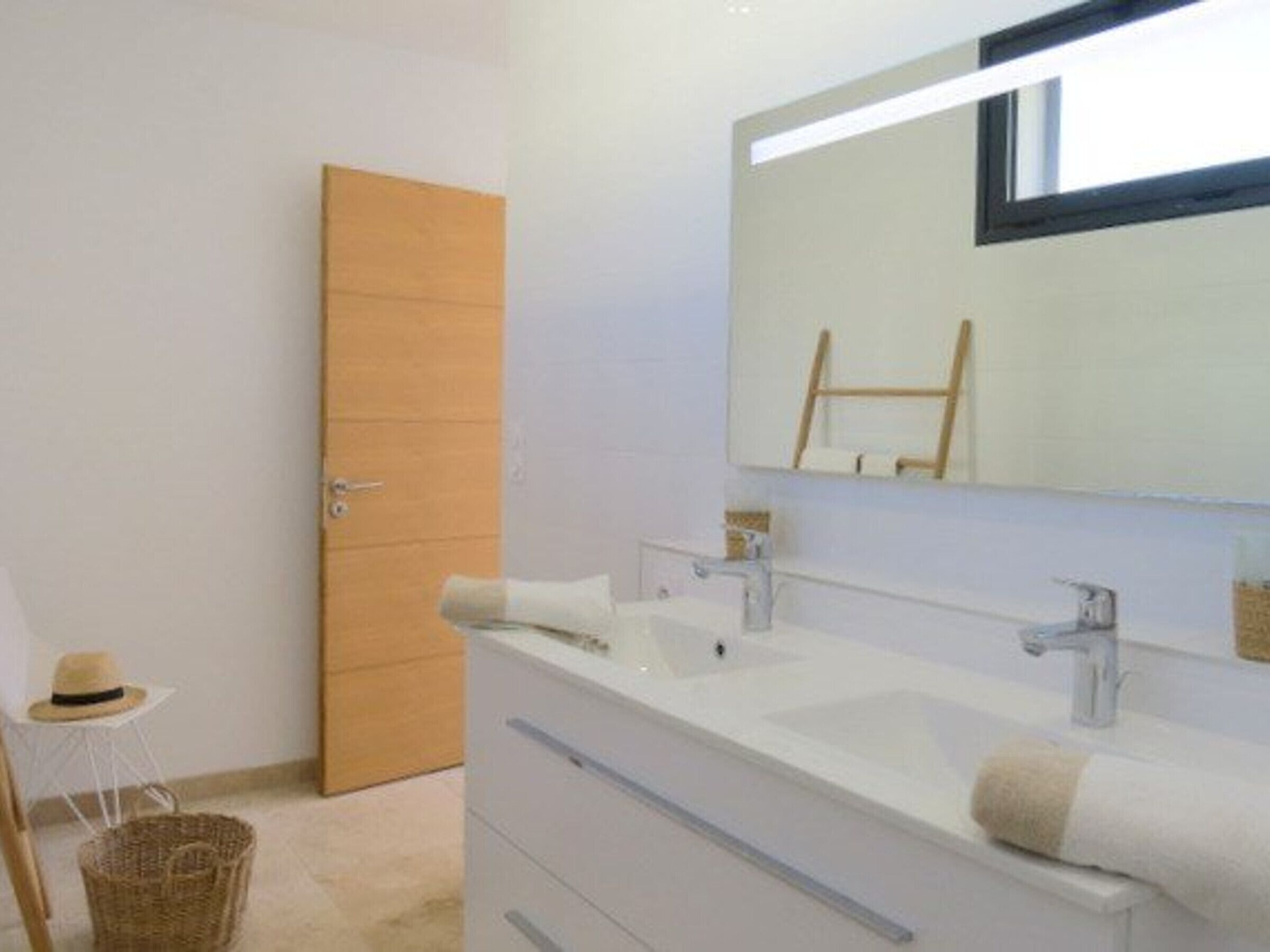 Un baño moderno con un espejo grande, dos lavamanos y una puerta de madera.