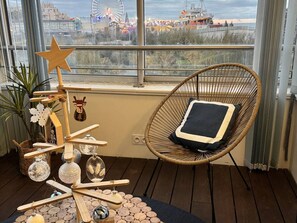 Une pièce chaleureuse avec une grande fenêtre donnant sur un parc d’attractions, un fauteuil en osier avec un coussin et une structure décorative en bois agrémentée d’ornements.