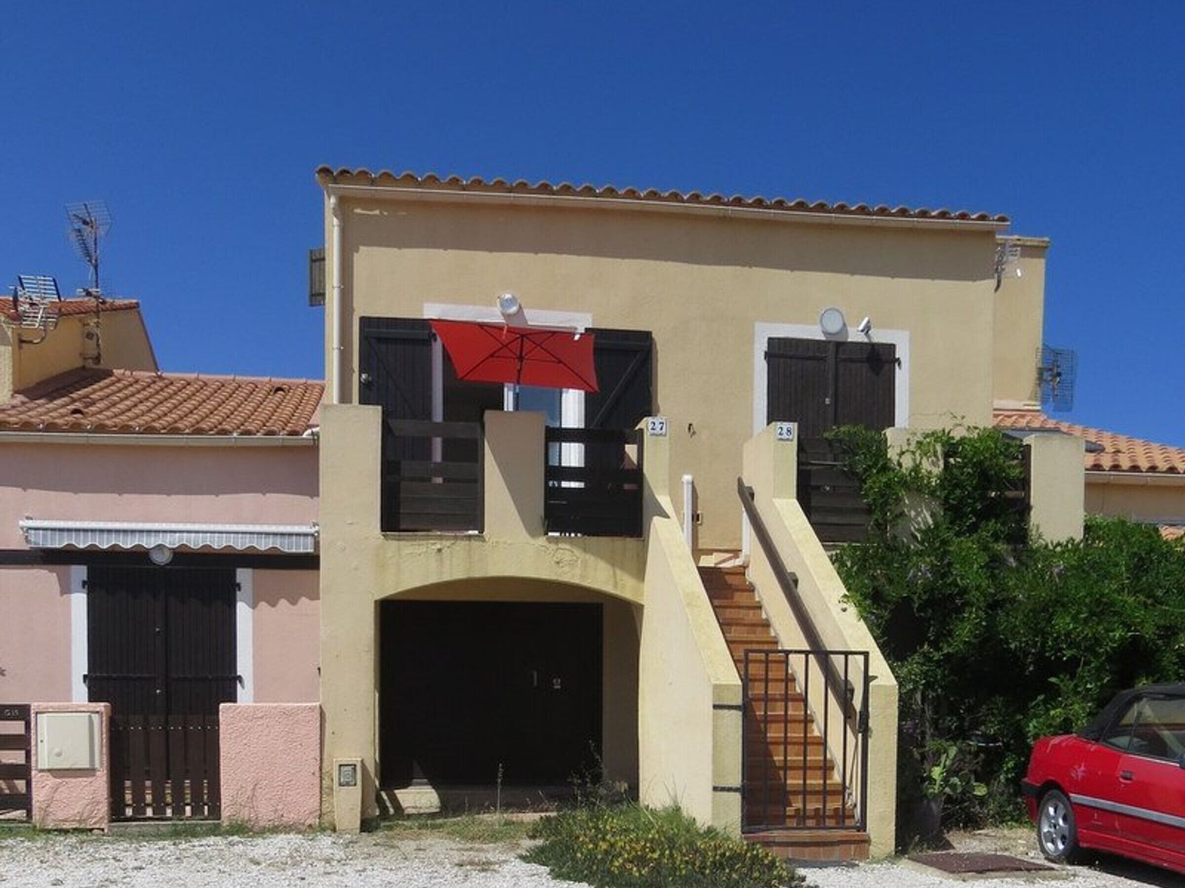 A two-story building with a beige facade, black shutters, and a red umbrella.