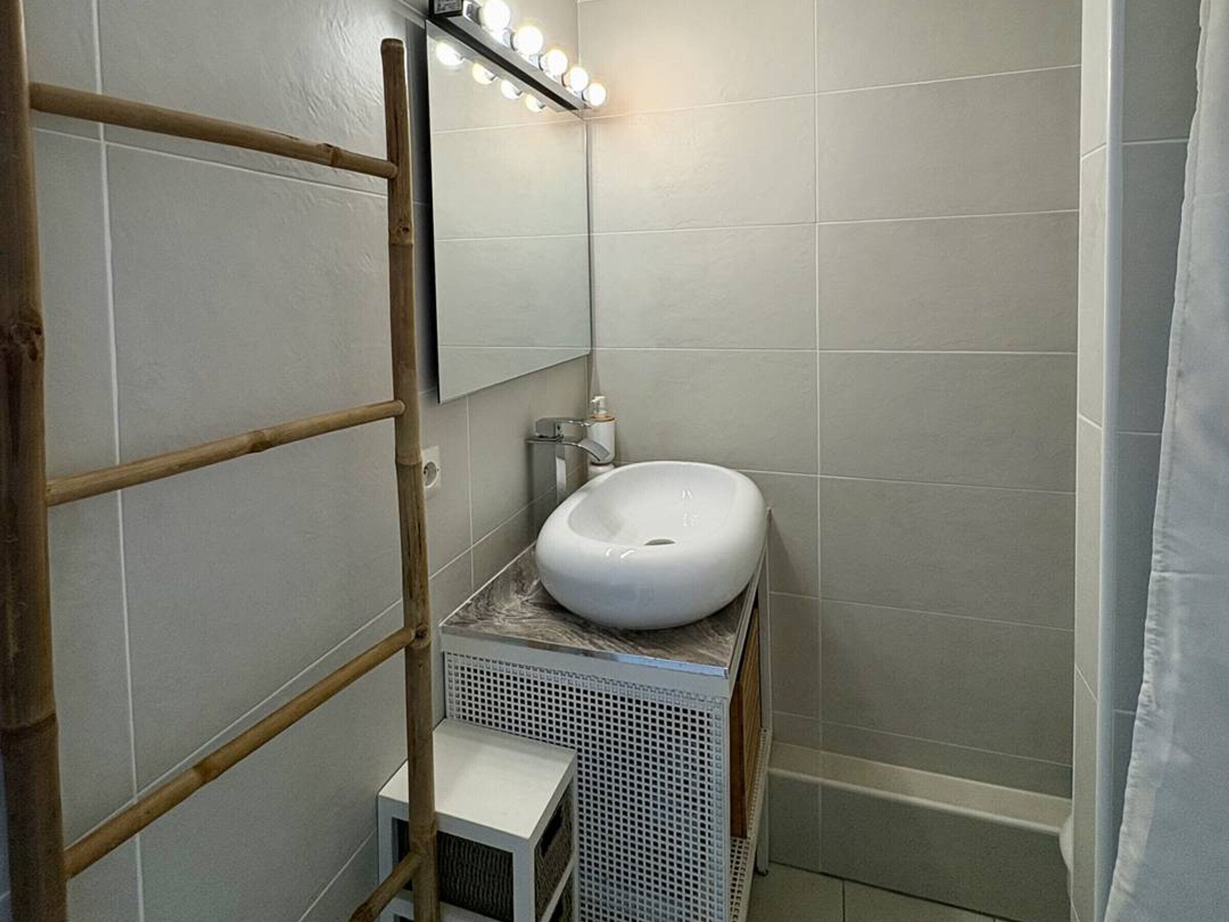 Une salle de bain avec un lavabo blanc, un miroir avec éclairage intégr é et un rideau de douche.
