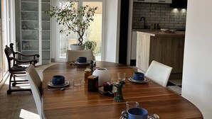 Comedor con una mesa de madera, sillas y una planta en maceta. Se ve una cocina al fondo.
