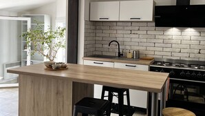 Una cocina moderna con una isla central, armarios blancos, salpicadero de ladrillo y una campana extractora negra.