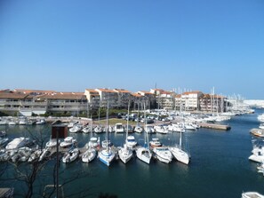 A marina with numerous boats docked, surrounded by multi-story buildings with red-tiled roofs. - Cozy Two-Room Apartment in Canet-Plage with Loggias and Parking (Canet-Plage)
