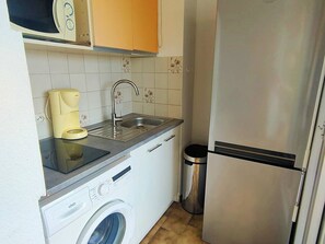 A compact kitchen with a washing machine, a coffee maker, a sink, and a stainless steel refrigerator. - Cozy Two-Room Apartment in Canet-Plage with Loggias and Parking (Canet-Plage)