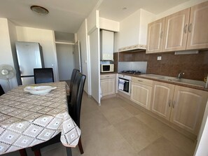 A compact kitchen with a dining table, chairs, a microwave, stove, and cabinets. - Renovated beachfront T3, loggia, private parking (Canet-Plage)