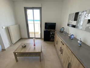 A modern living room with a wooden table, a TV, and a view of the beach through a sliding door. - Renovated beachfront T3, loggia, private parking (Canet-Plage)