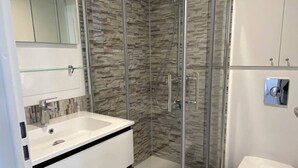 Ein modernes Badezimmer mit Duschkabine aus Glas, einem weißen Waschbecken und einer Toilette.