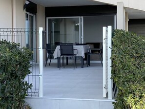 A modern outdoor dining area with a table and chairs, a sliding glass door leading to a covered patio, and a metal gate. - Renovated 1-bedroom with terrace, beach access, Canet-Plage (Canet-Plage)