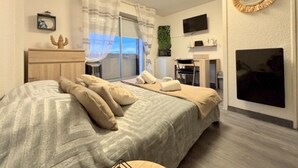 A bedroom with a bed, a desk, a chair, a TV, and a window with curtains. - Cozy studio beach access, balcony and parking (Le Barcarès)