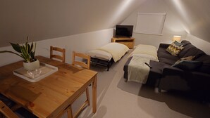 Ett mysigt sovrum på entresolplan med ett matbord i trä, två enkelsängar, en soffa, en tv och en krukväxt.