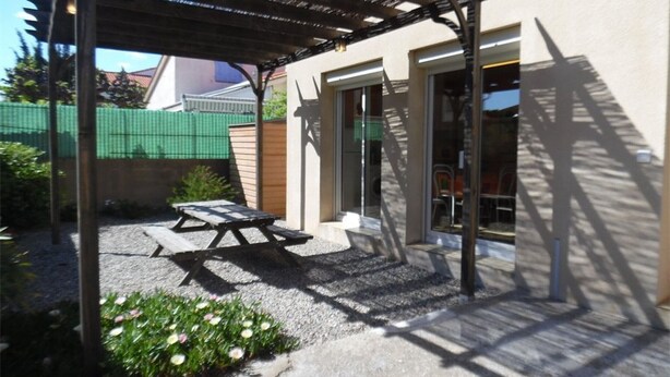 Un patio couvert avec une table et des chaises, une pergola et l’entr ée du bâtiment.