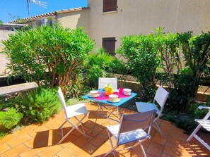 An outdoor patio with a table set for two, surrounded by greenery and a tiled floor. - Charming cottage Canet, near beach, quiet, private parking (Canet-en-Roussillon)