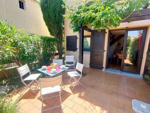 An outdoor patio with a table set for dining, surrounded by chairs, and a door leading to an interior space. - Charming cottage Canet, near beach, quiet, private parking (Canet-en-Roussillon)
