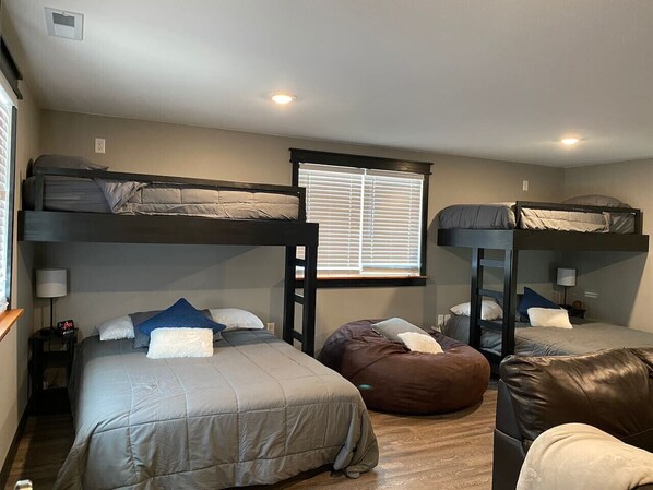 A dormitory-style room with bunk beds, a bean bag chair, and a small table with a lamp.
