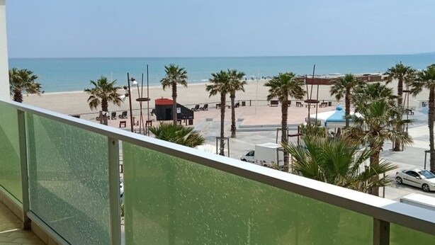 Un balcon avec vue sur une plage, des palmiers et un parking.