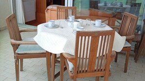 Une table ronde en bois, recouverte d’une nappe blanche, entourée de chaises en bois dotées de coussins.