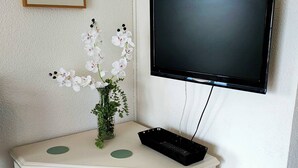 Valkoinen konsolipöytä, jonka päällä on valkoisten kukkien maljakko ja musta elektroninen laite.