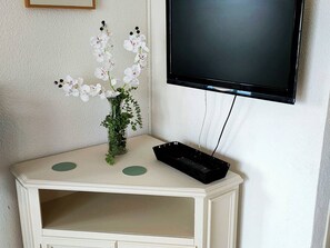 Ein weißer Konsolentisch mit einer Vase weißer Blumen und einem schwarzen elektronischen Gerät.