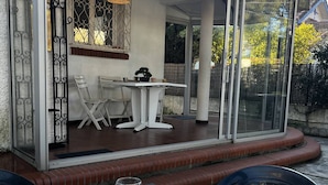 An outdoor patio with a table set for dining, a chair, and a glass door leading to a covered area with a table and chairs. - Single-storey air-conditioned house close to beach in Canet-en-Roussillon (Canet-en-Roussillon)