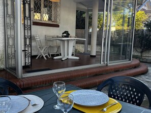 An outdoor patio with a table set for dining, a chair, and a glass door leading to a covered area with a table and chairs. - Single-storey air-conditioned house close to beach in Canet-en-Roussillon (Canet-en-Roussillon)