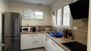 A compact kitchen with a stainless steel refrigerator, a microwave, a kettle, and a sink. There are cabinets with handles, a window with decorative glass, and a countertop with various items. - Single-storey air-conditioned house close to beach in Canet-en-Roussillon (Canet-en-Roussillon)