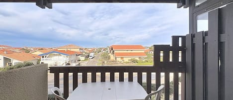 Un balcón con mesa y sillas, con vistas a una zona residencial con casas y una calle.