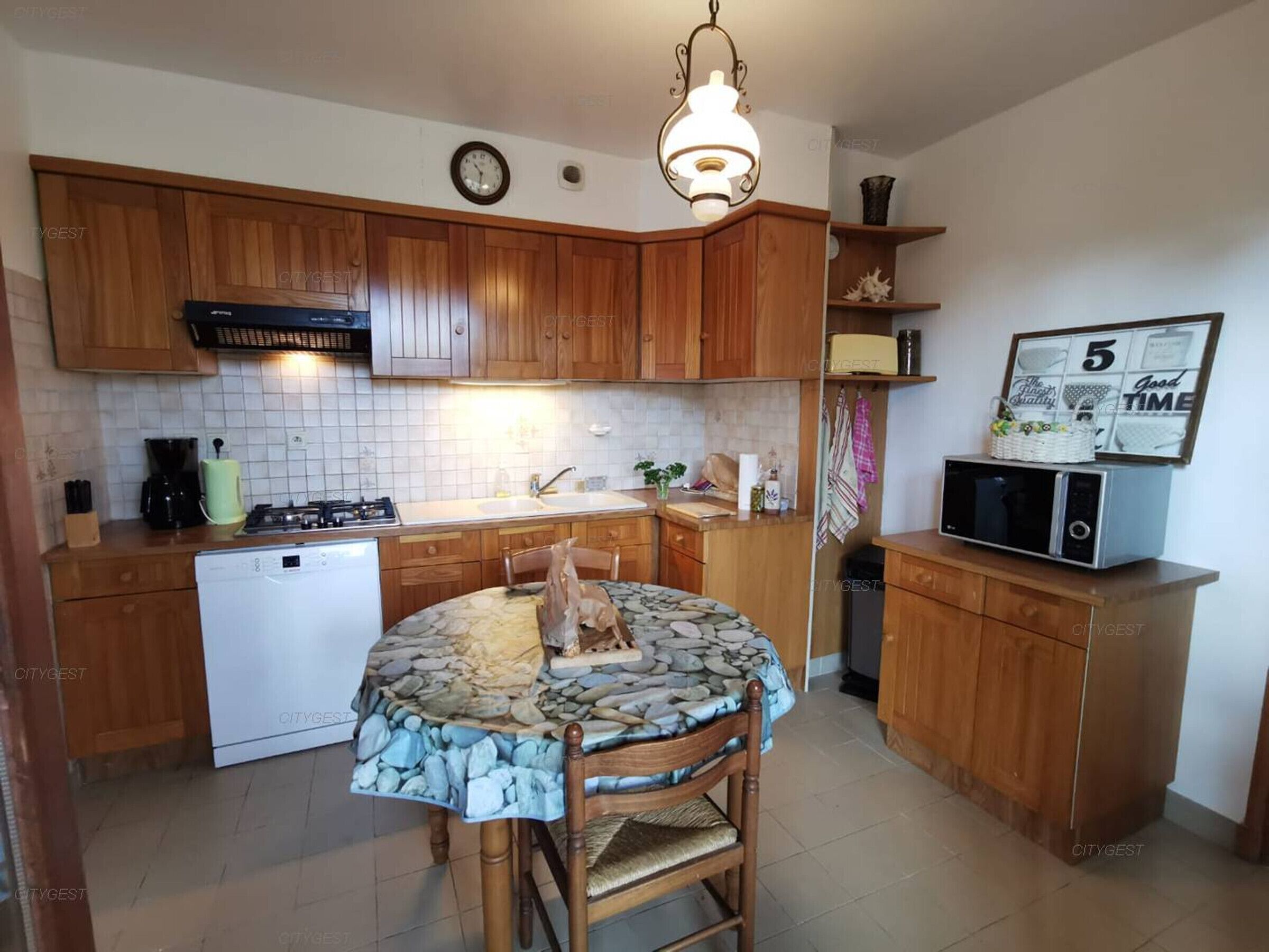 Une cuisine compacte avec des meubles en bois, une cuisinière à gaz, un lave-vaisselle et un four à micro-ondes.