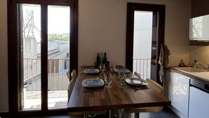 Een eetgedeelte met een houten tafel voor vier personen, een keuken met een vaatwasser, en uitzicht door grote schuifdeuren.