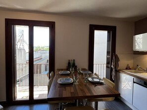 A dining area with a wooden table set for four, a kitchen with a dishwasher, and a view through large sliding doors. - T2 Apartment in Canet Plage, 4 Pers, Terrace, Close to Beach (Canet-en-Roussillon)