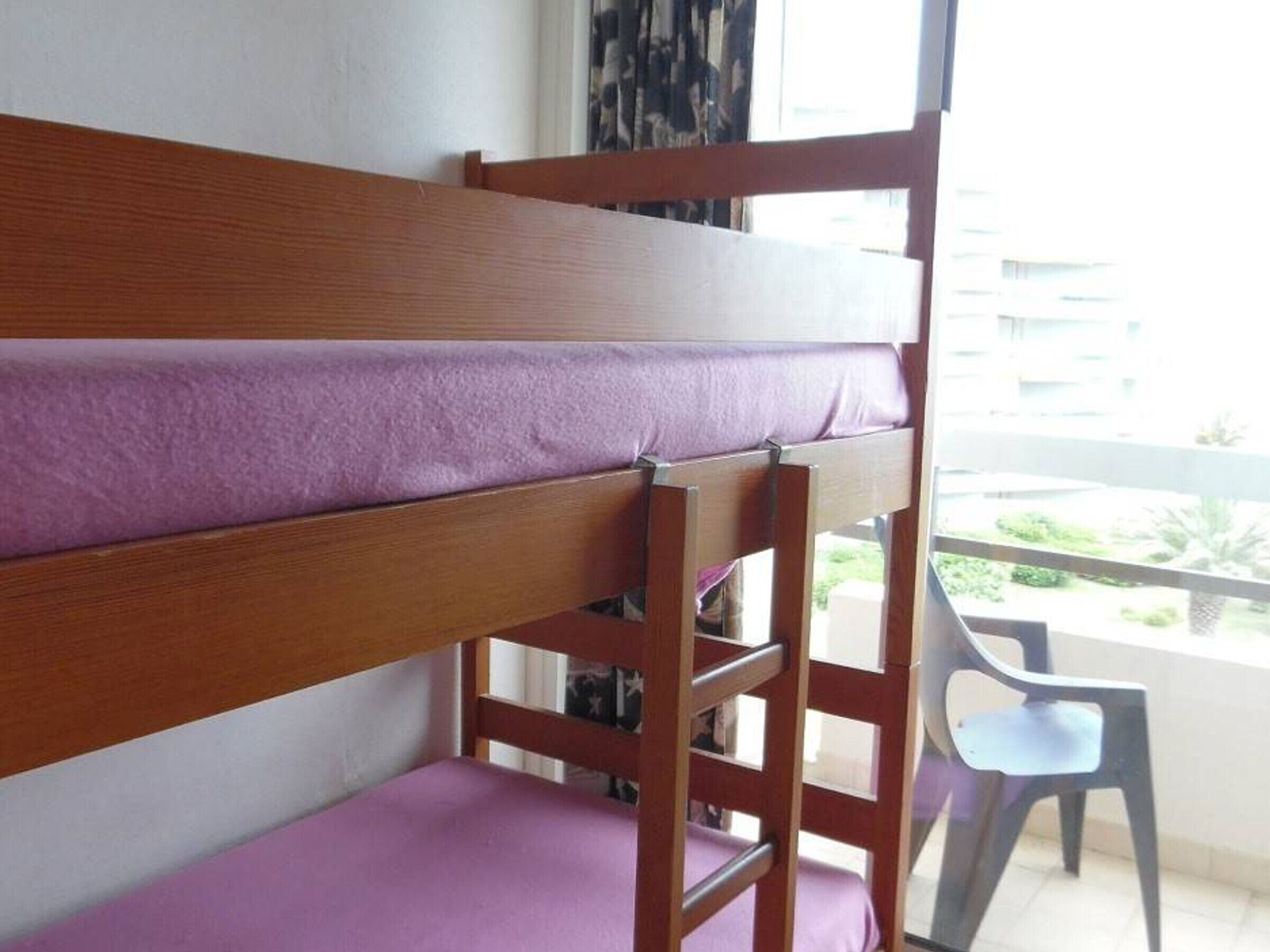 A bunk bed with a purple mattress in a room with a balcony.