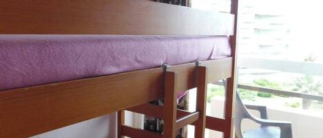 A bunk bed with a purple mattress in a room with a balcony.