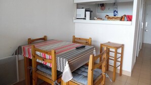 Pieni, viihtyisä huone, jossa on puinen pöytä ja tuolit, raidallinen vuodevaatteilla varustettu sänky, seinällä oleva kello sekä pieni keittokomero, jossa on mikroaaltouuni ja pieniä kodinkoneita.