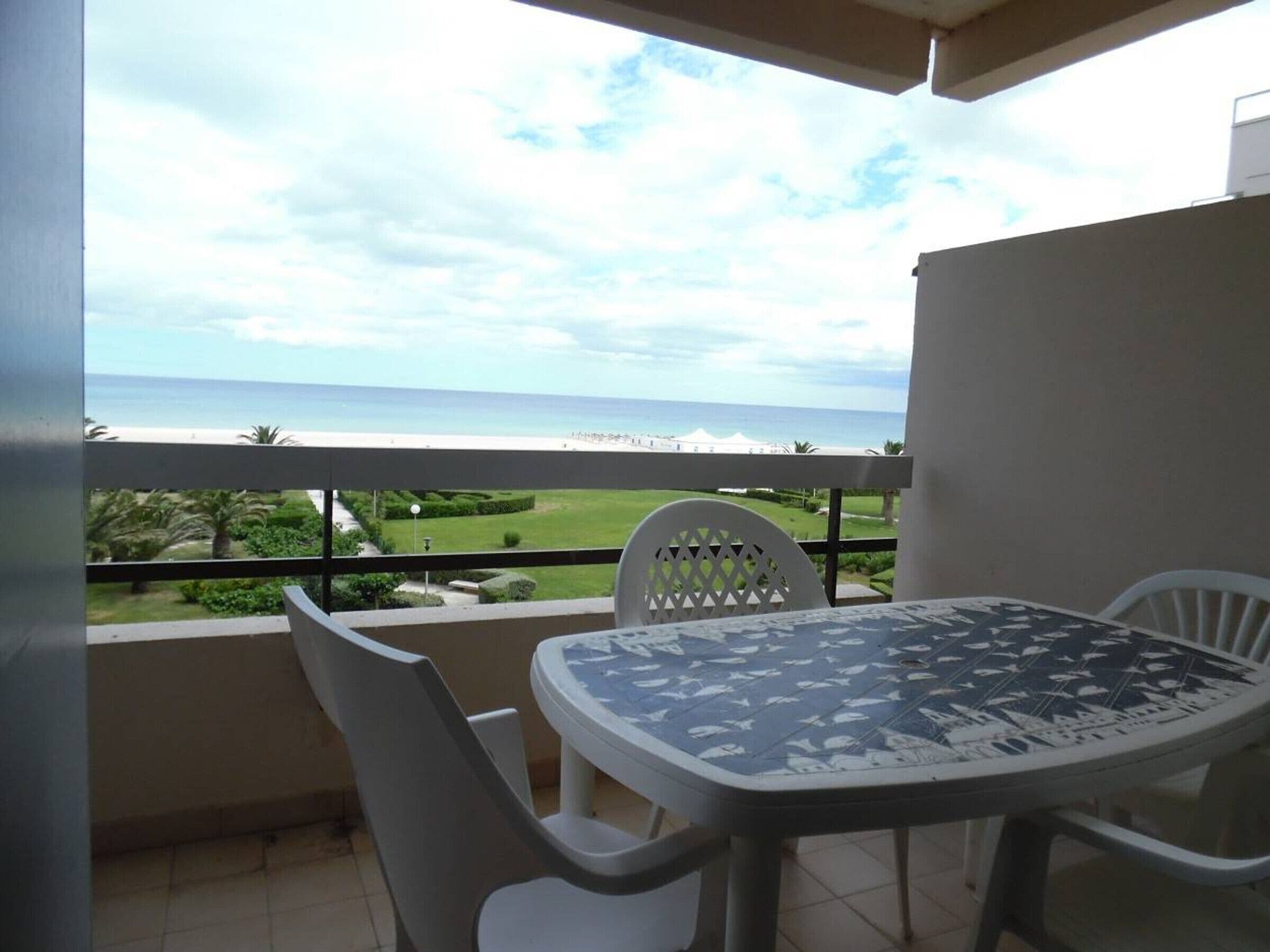Un balcon avec une table et des chaises, donnant sur une plage et un terrain de golf.