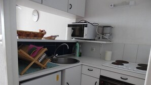 Pieni, käytännöllinen keittiö, jossa on valkoiset kaapit, mikroaaltouuni, pesuallas, liesi ja astianpesukone.