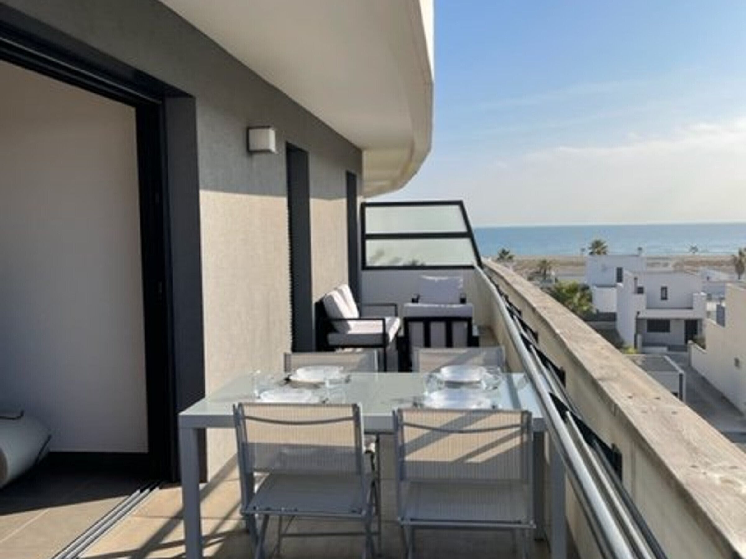 Un balcon avec une table et des chaises, donnant sur une plage et d’autres bâtiments.