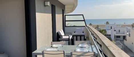 A balcony with a table and chairs, overlooking a beach and other buildings.