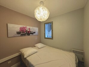 A bedroom with a bed, a wall-mounted artwork of pink flowers, a window with a view, and a unique ceiling light fixture. - Apartment for 4 with parking in Barcarès (Le Barcarès)