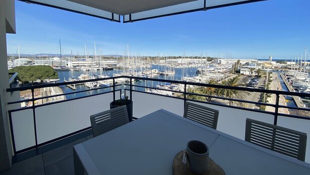 Een balkon met een tafel en stoelen, uitkijkend op een jachthaven met boten en jachten.