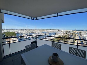 A balcony with a table and chairs, overlooking a marina with boats and yachts. - 4-star apartment with wifi and parking, steps from the beach (Canet-Plage)