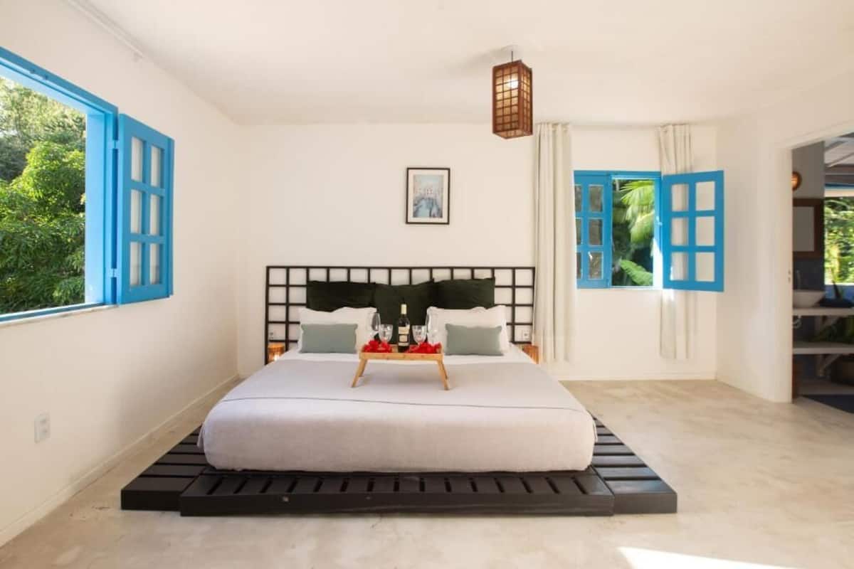Un dormitorio con cama, una mesita de noche con una bandeja de vasos y vistas al verdor exterior.