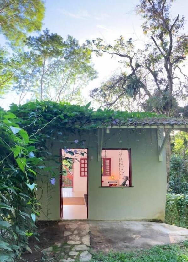 A small, rustic building with a stone foundation and a green roof, surrounded by lush greenery. - Casa Ryokan (Guaramiranga)
