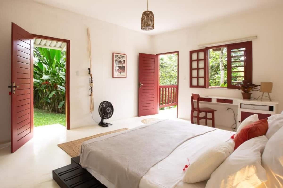 Un dormitorio con cama, escritorio y silla. Hay dos puertas, una abierta y otra cerrada.