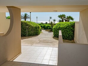 A paved pathway leading to a building entrance, flanked by neatly trimmed hedges and a clear view of the sky. - Modern apartment with air conditioning, balcony, and parking (Canet-en-Roussillon)
