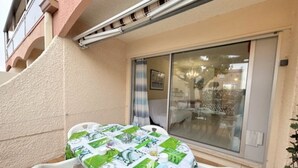 Pieni patio, jossa on pyöreä pöytä, jonka päällä on vihreä-valkoinen pöytäliina, kaksi valkoista muovituolia ja lasiliukuovi, joka johtaa sisätilaan.